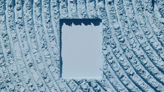 Overhead frame of a pale blue powder furrows surface with a rectangular shape pressed in, illuminated by orbiting directional light creating shadow movement