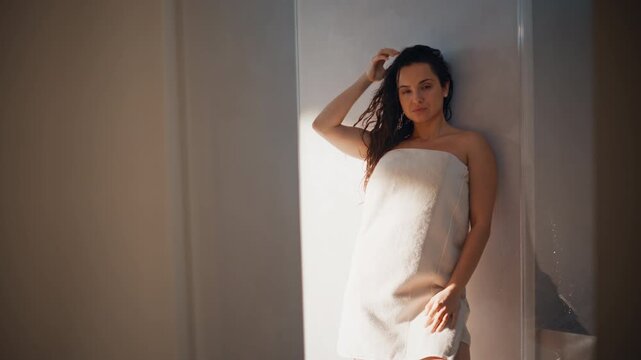 Woman relaxing in towel leaning sunlit bathroom wall, calm spa portrait