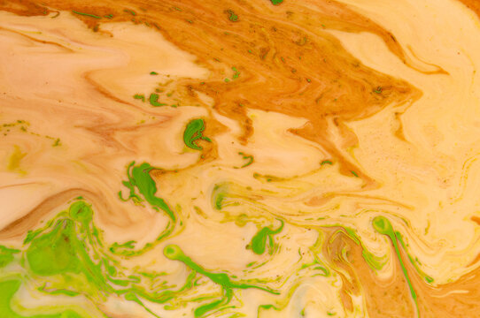 Swirls of brown and green colors mix in a vibrant pattern on a surface