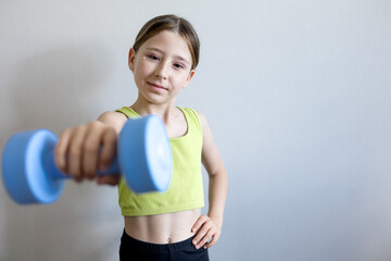 Naklejka premium Young girl holds blue dumbbell with focused expression