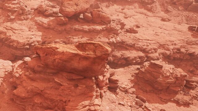 Rocks and terrain are visible on the surface of Mars. The landscape has a reddish hue. Dust covers parts of the ground. There are various rock formations scattered throughout the area.