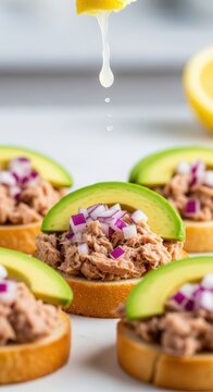 Delicious tuna tartare on crispy bread with fresh avocado and red onions, garnished with lemon juice for added flavor. Tasty tuna appetizer with vibrant green avocado and colorful garnishes.