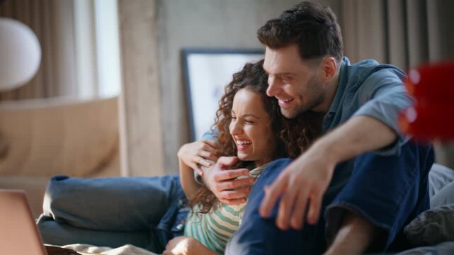 Couple embracing home sofa. Man hugging girlfriend watching laptop cozy weekend.