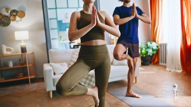 Couple practicing tree pose yoga together home living room. Morning meditation.