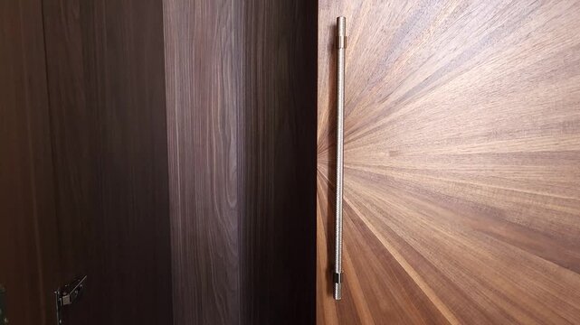 Woman's hand opening and then closing a luxury wooden wardrobe with a sunburst pattern design, showcasing the elegant gold handles and high quality craftsmanship of the modern furniture