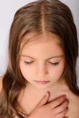 Fototapeta premium Close up portrait of beautiful little girl with closed eyes holding hand on her chest, top view