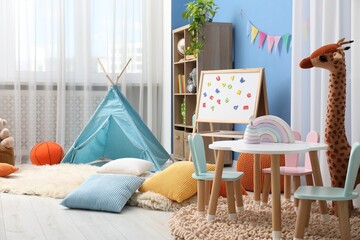 Small table with chairs, colorful pillows, wigwam, toys, shelving unit and magnetic board in stylish child's room. Interior design © New Africa