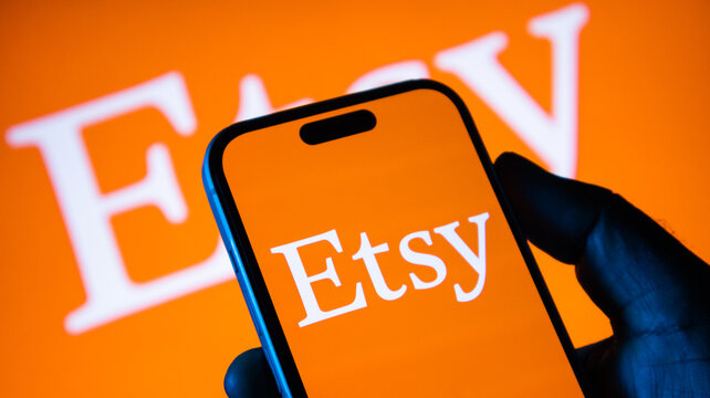 Person holding smartphone with etsy app logo displayed on screen against branded orange background.