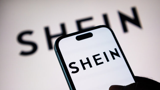 A close-up view of a hand holding a smartphone with the Shein logo prominently displayed on the screen.