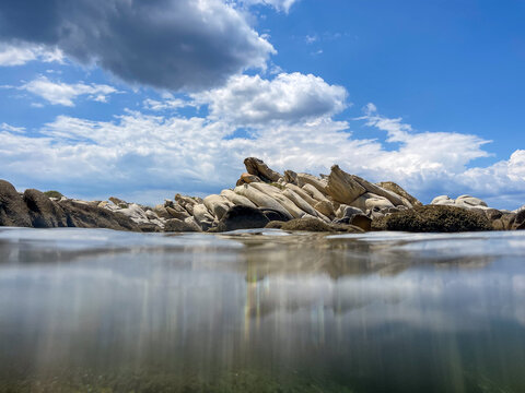 Smooth granite rock formations emerging from clear sea water for tropical coastal nature travel website design. Split water view of rocky shore and blue sky for summer vacation and resort mockups.
