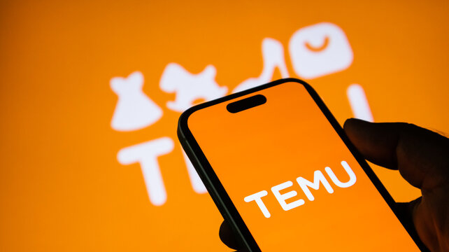 Temu shopping app logo displayed on smartphone held by hand with orange company background.