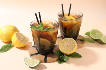 Fototapeta premium Refreshing ice tea with lime, lemon and mint in glasses on beige table, closeup