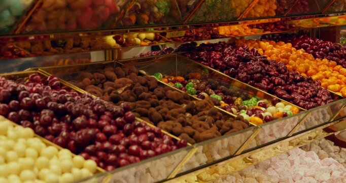 Close up of traditional Turkish delight confections arranged in metal bins at candy shop, featuring white, red, brown, yellow varieties coated in cocoa powder, nuts, sugar.