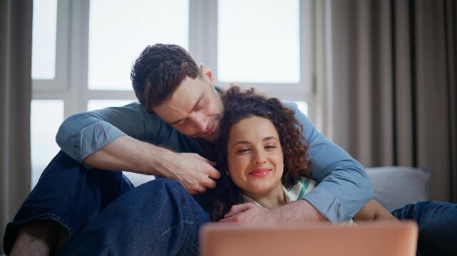 Man embracing girlfriend watching laptop home. Loving couple relaxing on sofa