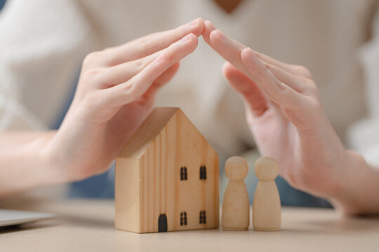 Home insurance concept. Hands protecting a wooden house and family figures, representing property protection and financial security. Home insurance, family, protection, security, property