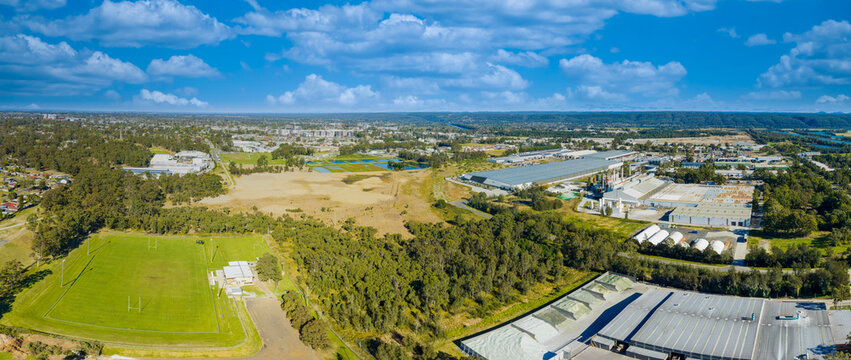 Drone aerial panoramic photograph of industrial buildings and a sports field surrounded by trees and foliage in the Greater Western Sydney town of Penrith in New South Wales, Australia