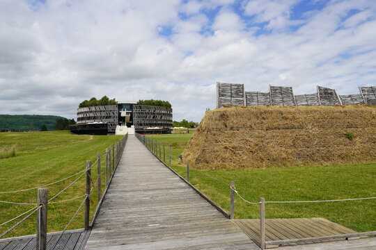 View from a reconstruction of Roman fortification lines to Mus&eacute;oParc&rsquo;s visitor center near Alise-Sainte-Reine (Alesia). Cylindrical building wrapped in a wooden herringbone facade. June, France.