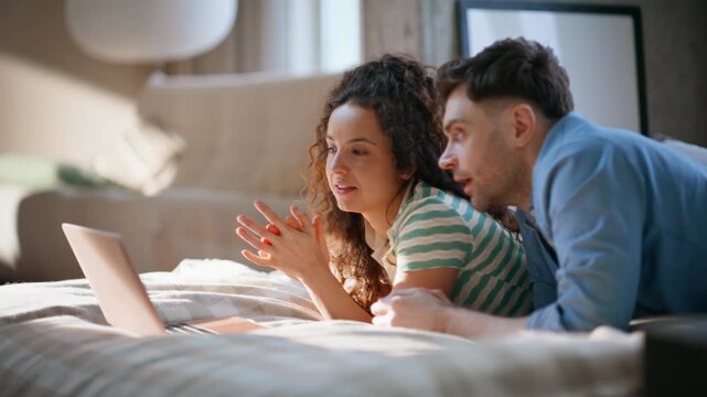 Loving couple laughing bed with laptop. Man woman resting cozy weekend home.