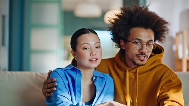 Multiethnic couple shopping online laptop home sofa. Reacting to website.