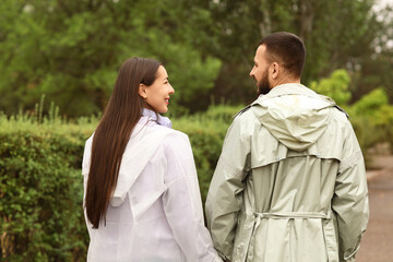 Fototapeta premium Young couple with raincoats in park, back view