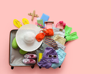 Composition with open suitcase, summer clothes, headphones, flippers and passport on pink background © Pixel-Shot