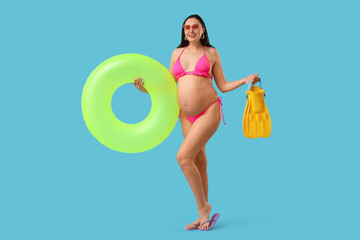 Young pregnant woman with inflatable ring and flippers on blue background. Traveling concept © Pixel-Shot