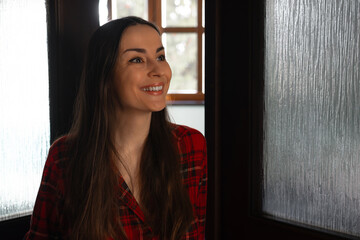 Fototapeta premium Happy woman smiling in doorway wearing plaid pajamas