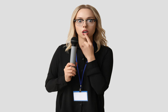 Portrait of curious female journalist with microphone taking interview on grey background
