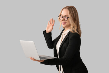 Beautiful young businesswoman with laptop waving hand on grey background © Pixel-Shot