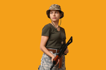 Fototapeta premium Confident young female soldier with assault rifle on yellow background