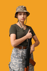 Fototapeta premium Confident young female soldier with assault rifle on yellow background