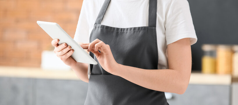Person in a gray apron using a digital tablet for online ordering and inventory management in a modern kitchen, a person wearing a gray apron and white t-shirt uses a digital tablet