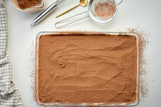 Tiramisu dessert is covered with cocoa powder in glass baking dish
