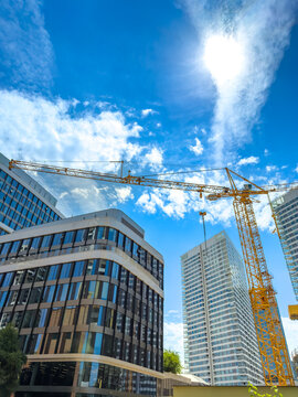 Construction activity under bright sky. A construction site is active with a crane. Tall buildings surround the area. The sky is clear with some clouds.