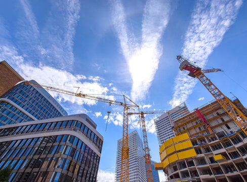 Construction cranes work in city center. Cranes stand tall against a blue sky as workers build new structures in a busy city center during the day.