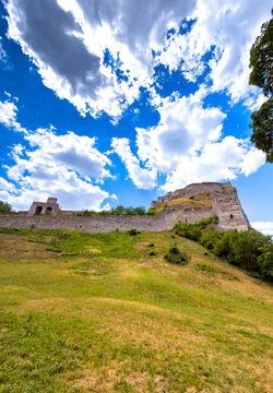 Old castle on a hill under a blue sky. A castle stands on a green hill, with clouds floating in a bright sky. The scene shows nature around the ruins.