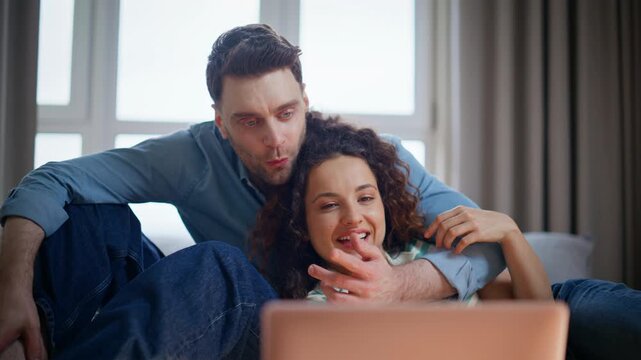 Happy couple watching laptop together home. Man embracing girlfriend on couch