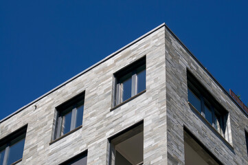 Modern building facade with grey stone cladding under blue sky © Marlon