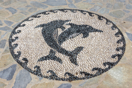 Traditional Greek pebble mosaic featuring two dolphins made of marine peba stone pavement in Greece 

Round black and white stone artwork depicting dolphins made of marine pebbles in Greece