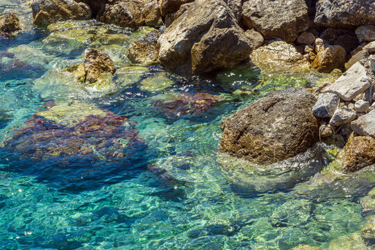 Transparent ocean water and rocky seabed under bright summer sunlight in Greece