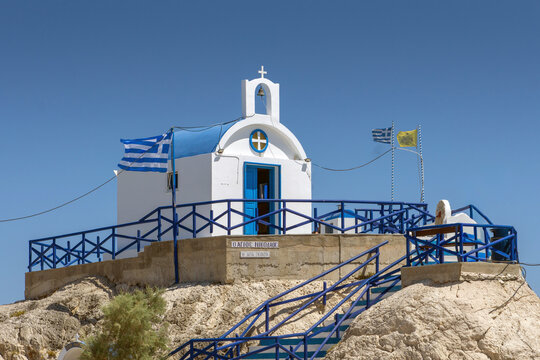 Traditional white and blue Greek Orthodox chapel with national flag on a cliff in Kolymbia Rhodes under a clear sunny sky