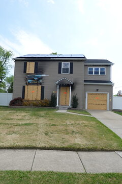 Vertical view of an abandoned fire damaged house with boarded windows and solar panels on its roof, set in a suburban environment. The atmosphere conveys disaster, neglect and damage. The scene is wel