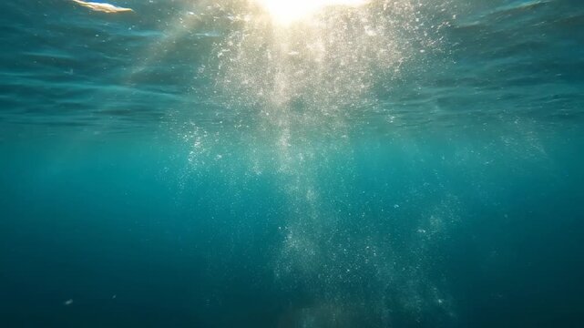 Sunlight rays penetrate the deep turquoise ocean surface, sparking a vibrant dance of oxygen bubbles as they rise through the tranquil water towards the shimmering glowing brilliance above