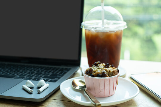 Close-up of Hot coffee latte with latte art milk foam in cup mug and Homemade Banana cup cake with laptop computer on wood desk office desk in coffee shop at the cafe,during business work concept