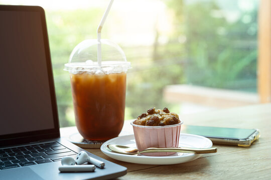 Close-up of Hot coffee latte with latte art milk foam in cup mug and Homemade Banana cup cake with laptop computer on wood desk office desk in coffee shop at the cafe,during business work concept