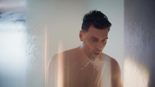 Man singing in shower holding showerhead like microphone. Happy guy bathing
