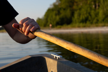 Close-up of a rower's hand gripping a paddle on an old boat during a sunset ride across a peaceful lake. © workszop