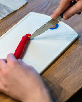 Knife cutting end of long red pepper on white board