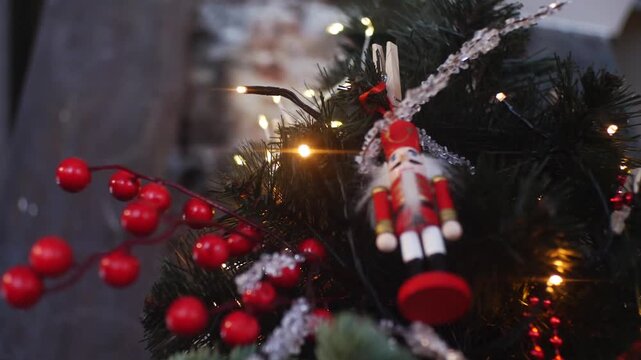 Closeup of a decorative nutcracker ornament hanging on a christmas tree with red berries and warm fairy lights in the background