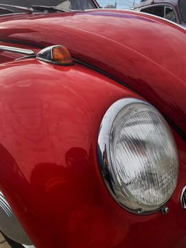 Close up of a shiny red vintage car round headlight and chrome indicator light on curved fender